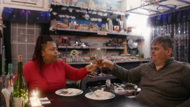 Een vrouw links aan tafel en man rechts aan tafel proosten bij hun avondeten.