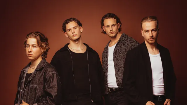 bandfoto van New Dawn. 4 jongens in het zwart gekleed tegen een oranje achtergrond