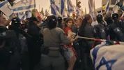 Nava Rozolio,een van de protestleiders. Er is een demonstratie met Israëlische vlaggen en politie op een drukke straat.