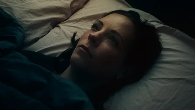 Een vrouw staart naar het plafond in een donkere kamer in bed