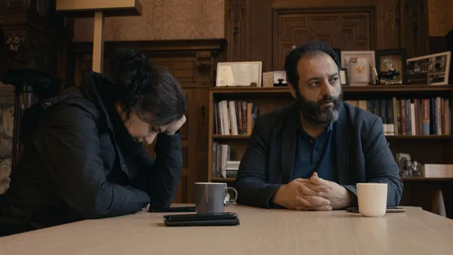 Annsar en Uğur zijn in gesprek. Ze zitten aan een houten tafel met kopjes drinken voor ze.
