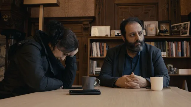 Annsar en Uğur zijn in gesprek. Ze zitten aan een houten tafel met kopjes drinken voor ze.