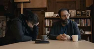 Annsar en Uğur zijn in gesprek. Ze zitten aan een houten tafel met kopjes drinken voor ze.