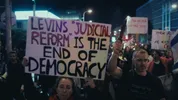 Demonstranten lopen op straat in Tel Aviv, ze hebben allemaal bordjes met demonstratie teksten er op.