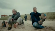 Arnaut en acteur als Albert Einstein trekken schoenen aan op strand.