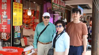 Pete en zijn ouders staan in winkelstraat waar verschillende Chinese winkels, etalages en reclame borden te zien zijn.