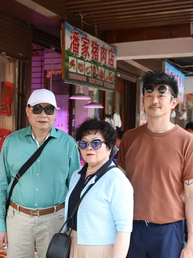 Pete en zijn ouders staan in winkelstraat waar verschillende Chinese winkels, etalages en reclame borden te zien zijn.