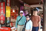 Pete en zijn ouders staan in winkelstraat waar verschillende Chinese winkels, etalages en reclame borden te zien zijn.