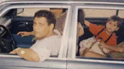 Een oude foto in een auto waar een man en een kind in zitten.