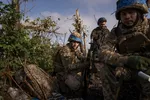 Drie jonge militairen in camouflagepakken naast een struik.
