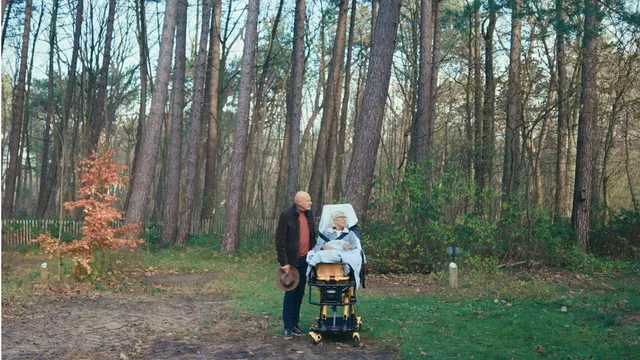Midden in een bos staat een oude man naast een vrouw in een ziekenhuisbed