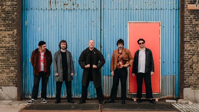 De leden van de band staan voor een blauwe muur