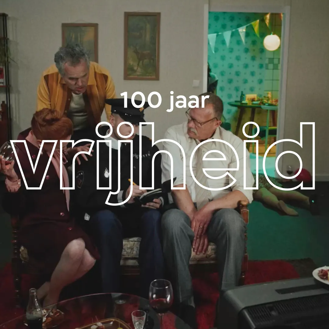 Een familie die in een huiskamer op banken zit en naar een televisie kijkt. Ook staat de tekst 100 jaar vrijheid in beeld.