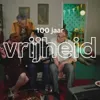 Een familie die in een huiskamer op banken zit en naar een televisie kijkt. Ook staat de tekst 100 jaar vrijheid in beeld.