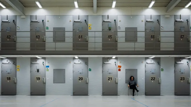 Een cel met gesloten deuren en een vrouw op een stoel.