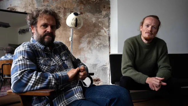 Jaap van Heusden en Jefta Varwijk zitten in een kantoorruimte op de bank en kijken de camera in.