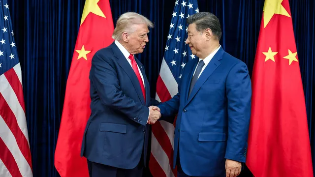Een witte man met blond haar en rode stropdas schudt de hand van een Oost-Aziatische man met lichtbruine huid en grijszwart haar. Achter hen staan Amerikaanse en Chinese vlaggen.