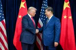 Een witte man met blond haar en rode stropdas schudt de hand van een Oost-Aziatische man met lichtbruine huid en grijszwart haar. Achter hen staan Amerikaanse en Chinese vlaggen.