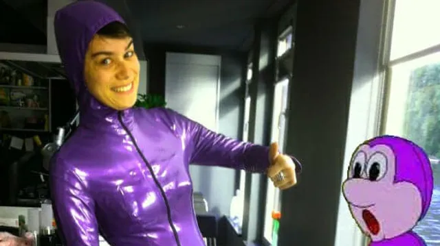 Een witte vrouw in een glimmend paars pak poseert lachend met een duim omhoog naast een getekende Purno de Purno. Onderaan staat in grote paarse letters: "SAPPEREDOSIO!".