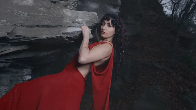 Naaz in een rode jurk hangend aan een rots