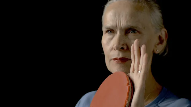 Tafeltennisster Bettine Vriesekoop kijkt geconcentreerd voor zich uit, in haar linkerhand houdt ze een tafeltennisbatje gereed, haar rechterhand houdt ze tegen het batje aan.