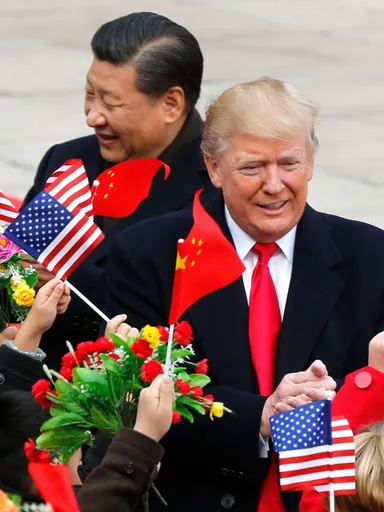 De president van de Verenigde Staten en de partijleider van China lopen tussen kinderen die Chinese en Amerikaanse vlaggetjes en bloemen omhooghouden.