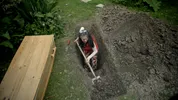 Adelheid Roosen staat in een tuin en graaft met een schop een kistdiep gat in de grond. Links naast haar ligt een houten kist. Om haar heen is opgegraven aarde zichtbaar. Een still uit het tv-programma Roosen&Borst.