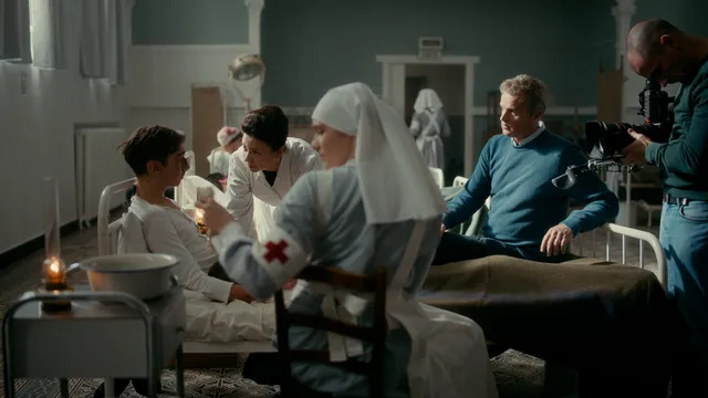 Filmopname in ziekenhuisscène met verpleegsters, patiënt en cameraman.