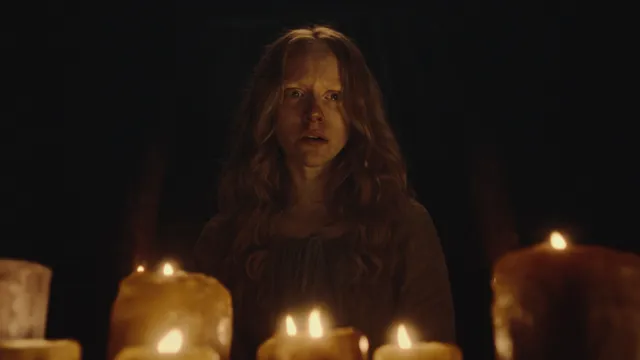 brandende kaarsen op de voorgrond met daarachter een vrouw die huilend en geschrokken vooruit staart.
