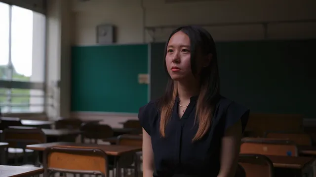 Een vrouw die bij een tafel in een klaslokaal zit.