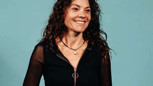 Vrouw met zwart krullend haar tegen mintgroene achtergrond. Ze kijkt lachend naar rechts