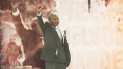 Een zwarte man in pak met grijs haar houdt zijn vuist omhoog.