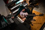 Een man in een muziekstudio achter een laptop met een basgitaar op schoot
