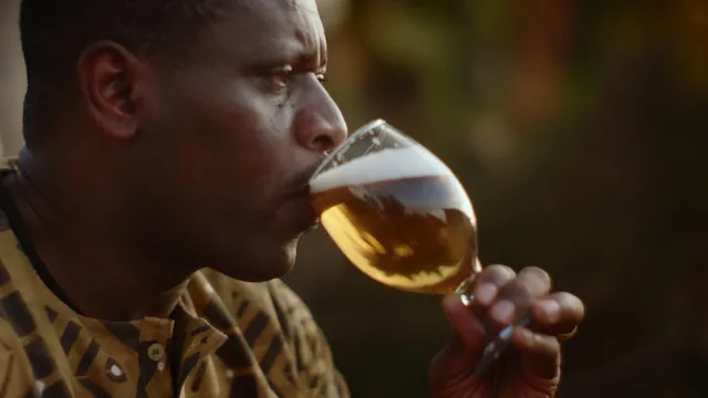 Foto van John Kavakure die een biertje drinkt