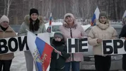 Vier vrouwen in winterjassen houden een leus in cyrillisch schrift omhoog. Tussenin staat een klein jongetje met wintermuts op, hij houdt een Russische vlag vast.