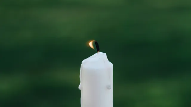 Foto van een brandende witte kaars tegen een groene achtergrond