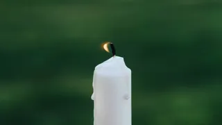 Foto van een brandende witte kaars tegen een groene achtergrond