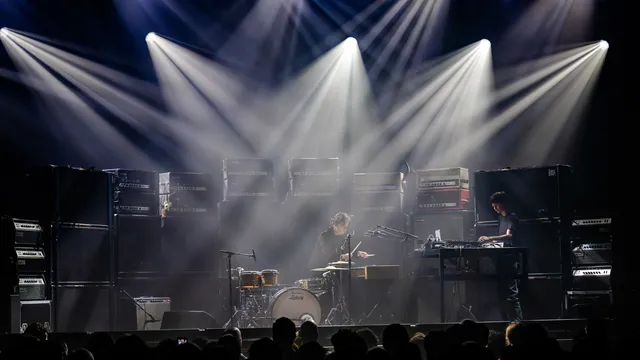 Twee muzikanten op een podium dat volgebouwd is met gitaarversterkers