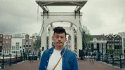 Pete staat voor een brug in Nederland, op de achtergrond zijn huisjes te zien.