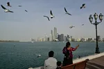Een vrouw voedt meeuwen langs een promenade met uitzicht op de skyline van Abu Dhabi