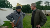 Man in historisch militair kostuum praat met Arnaut in moderne jas op kampement.