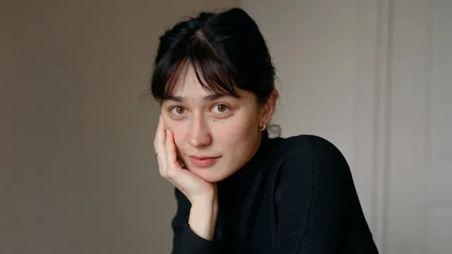 Een vrouw, gekleed in een zwarte coltrui, kijkt in de camera