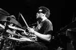 Foto van de drummer van Iguana Death Cult die achter zijn drumstel zit. Hij tuit zijn lippen en bespeelt met duidelijk passie de drums
