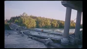 Een verwoeste brug over een rivier, met een persoon tussen de brokstukken en bomen op de achtergrond.
