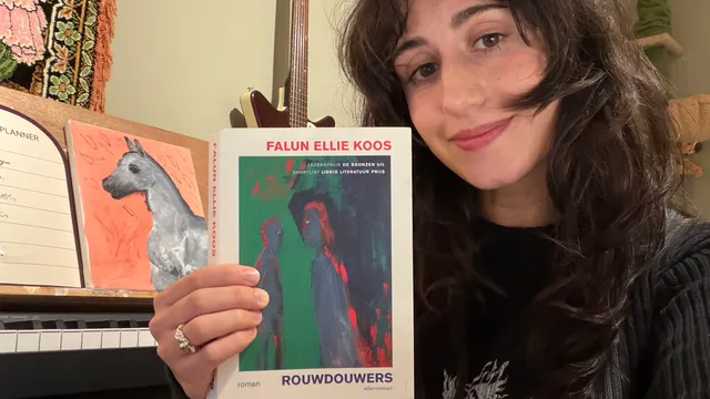 Naaz houdt het boek Rouwdouwers naast haar hoofd in de lucht.