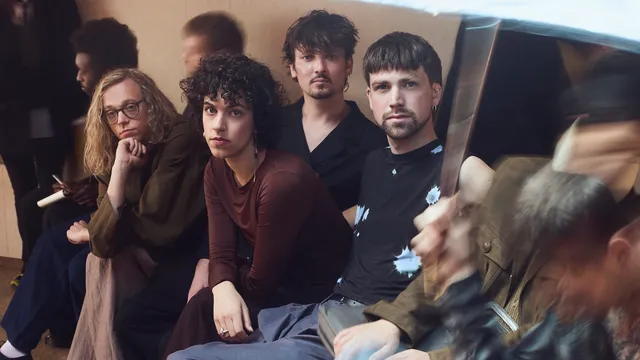 Band Ao naast elkaar op een bankje tussen drukke mensen