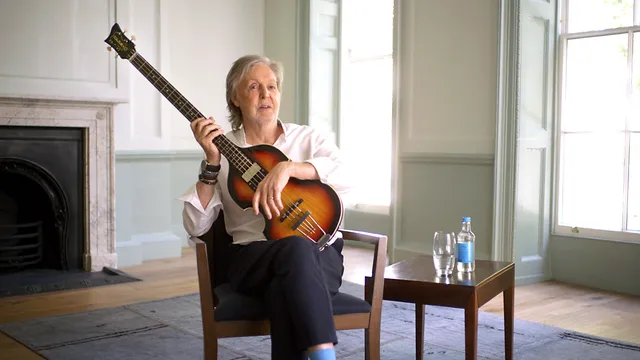 Paul McCartney zit op een houten stoel met basgitaar op zijn schoot
