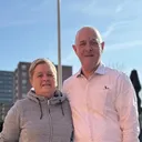 Ton en Loes staan naast elkaar met een arm om elkaar heen, ze kijken in de camera.