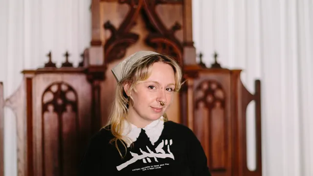 Persoon met neusringetje voor een soort houten kerkmeubel