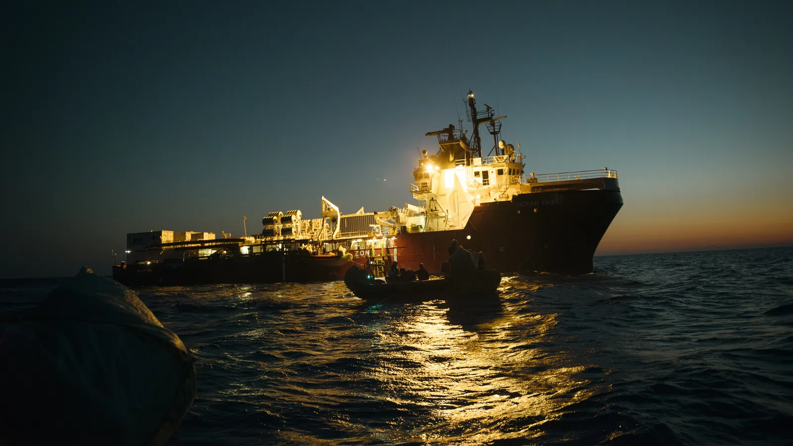 Een groot reddingsschip 's nachts op zee, met een kleine reddingsboot op de voorgrond.